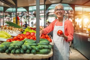 Apartments in Lebanon Market vendor smiling while holding fresh tomatoes at a produce stall.