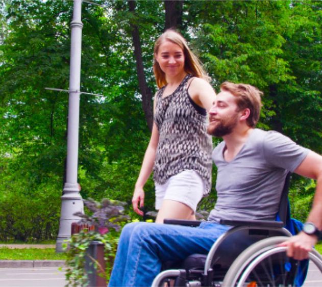 Apartments in Lebanon A woman standing behind a man in a wheelchair, both smiling and enjoying time outdoors.