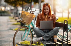 Apartments in Lebanon A woman with red hair working on a laptop while sitting on a park bench next to her bicycle.