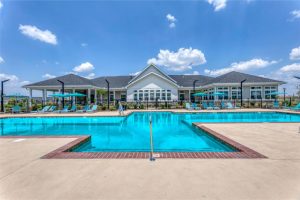 Apartments in Lebanon, IN Outdoor swimming pool with clear blue water, surrounded by lounge chairs, sun umbrellas, and a well-maintained large building in the background under a partly cloudy sky.