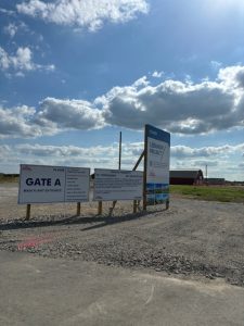 Apartments in Lebanon, IN Entrance signage at a construction site labeled "Gate A, Main Plant Entrance." Several boards display site rules and project details for Optimal Living for Eli Lilly's Biotech Professionals under a partly cloudy sky.