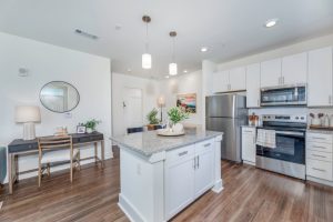 Apartments in Lebanon, IN Modern kitchen with stainless steel appliances, white cabinets, and granite countertops. A small dining area with a wooden table and chairs is adjacent. The room is well-lit with ceiling lights.