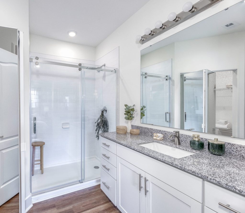 Indiana, Boone County, Lebanon Apartments for rent A modern bathroom featuring a glass-enclosed shower, a vanity with a granite countertop, a sink, and a large mirror with light fixtures above. Wood flooring and white cabinetry complete the space. See all available apartments for rent at Hickory Cottages in Indiana Boone County Lebanon, Hickory Cottages has rental units ranging from 664-1420 sq ft