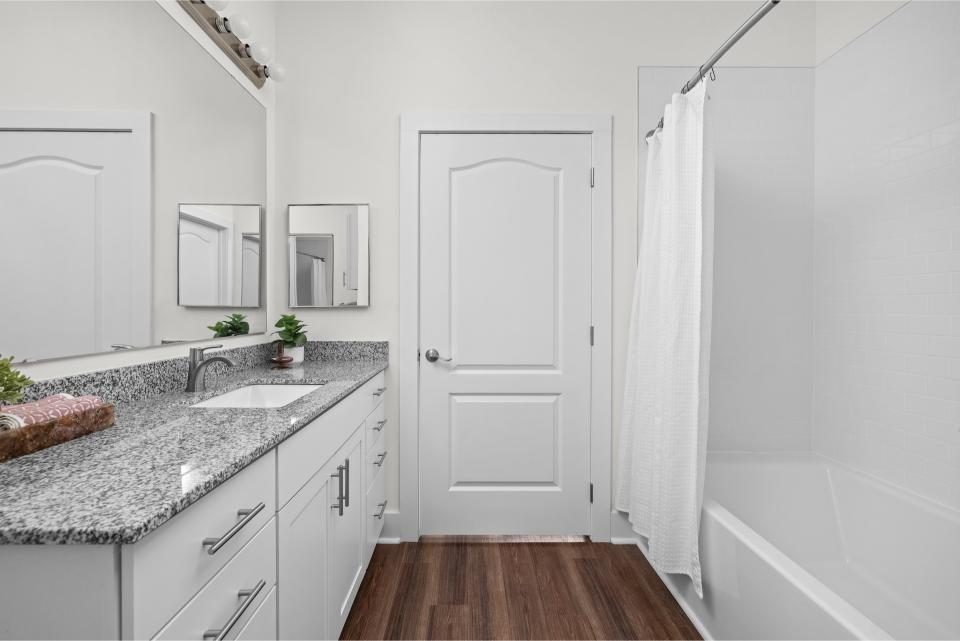Indiana, Boone County, Lebanon Apartments for rent A modern bathroom with white walls, a granite countertop, undermount sink, white cabinets, a bathtub with a white shower curtain, and wood-look flooring. See all available apartments for rent at Hickory Cottages in Indiana Boone County Lebanon, Hickory Cottages has rental units ranging from 664-1420 sq ft