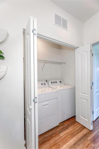 Apartments in Lebanon, IN A small laundry area with white washer and dryer units inside a closet with open double doors, white walls, and wood flooring.