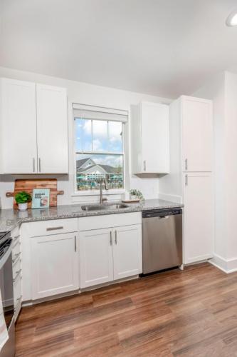 Apartments in Lebanon, IN Modern kitchen with white cabinets, granite countertops, stainless steel dishwasher, and hardwood flooring. A window above the sink lets in natural light, with a view of a building outside.