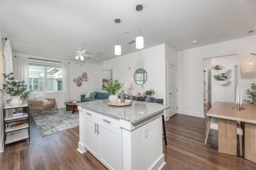 Apartments in Lebanon, IN Modern open-concept living room and kitchen with granite island, wood flooring, white walls, and contemporary furnishings. Dining area visible in the background with a light wood table and pendant light.