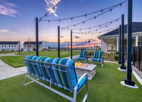 Apartments in Lebanon, IN Outdoor seating area with striped cushions around a fire pit, string lights overhead, on a lawn with houses and a sunset in the background.