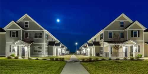 Apartments in Lebanon, IN A well-lit pathway leads between two parallel rows of modern townhouses under a clear night sky with a visible moon.