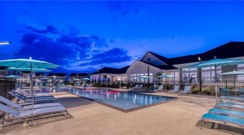 Apartments in Lebanon, IN Outdoor swimming pool area with lounge chairs and umbrellas at sunset, surrounded by modern buildings with illuminated windows.