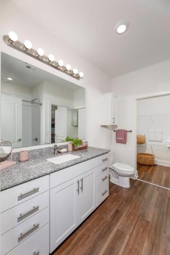 Apartments in Lebanon, IN Modern bathroom with a large mirror, granite countertop, vanity lights, white cabinets, a toilet, and a shower. The floor is wood-paneled, and there is a neatly arranged towel and basket.