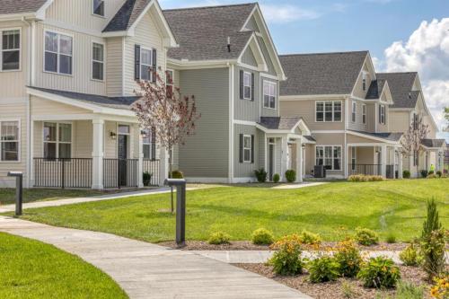 Apartments in Lebanon, IN A row of modern two-story houses with well-maintained lawns and flower beds, situated along a curved sidewalk on a sunny day.