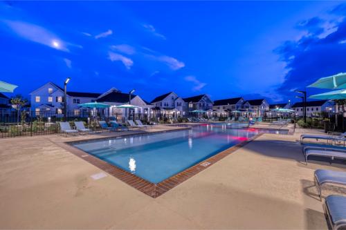 Apartments in Lebanon, IN Outdoor swimming pool surrounded by lounge chairs and umbrellas in front of a row of residential buildings during dusk.