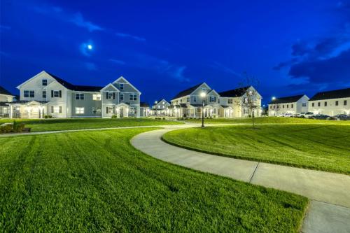 Apartments in Lebanon, IN Neighborhood view at dusk showing well-lit townhouses, a curved walkway, and neatly maintained grassy areas under a clear, moonlit sky.