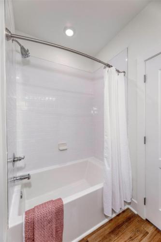 Apartments in Lebanon, IN A bathroom has a white bathtub with white tile walls, a white shower curtain, and a red towel draped over the side. There is a curtain rod with a corner showerhead above the tub. The floor is wooden.