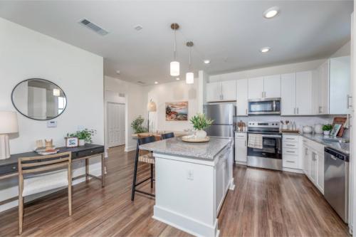 Apartments in Lebanon, IN A modern kitchen with stainless steel appliances, a central island with granite countertops, white cabinetry, and wooden flooring. A dining area with a table and chairs is visible in the background.