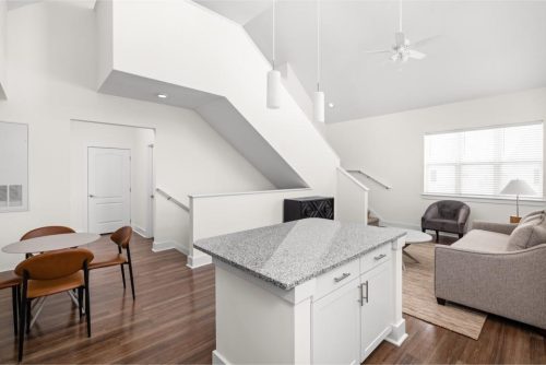 Indiana, Boone County, Lebanon Apartments for rent Modern open-concept living space with a kitchen island, dining table, sofa, armchairs, and staircase, featuring white walls and wood flooring. See all available apartments for rent at Hickory Cottages in Indiana Boone County Lebanon, Hickory Cottages has rental units ranging from 664-1420 sq ft