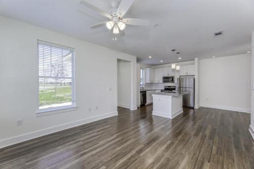 Apartments in Lebanon, IN Open-concept kitchen and living area with hardwood floors, white walls, and a ceiling fan. The kitchen features white cabinetry, stainless steel appliances, and pendant lighting over the island.