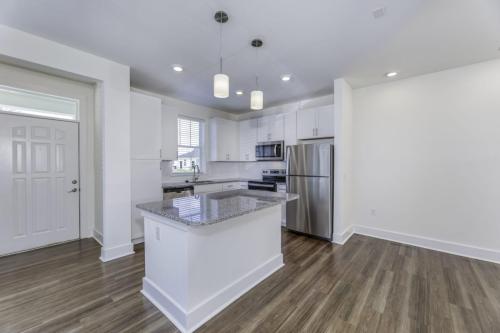 Apartments in Lebanon, IN Modern kitchen with stainless steel appliances, white cabinetry, an island with a granite countertop, wood flooring, recessed lighting, and a nearby door leading to another room.