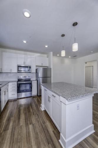 Apartments in Lebanon, IN Modern kitchen with stainless steel appliances, white cabinets, granite countertops, hardwood floors, and two pendant lights above a central island.