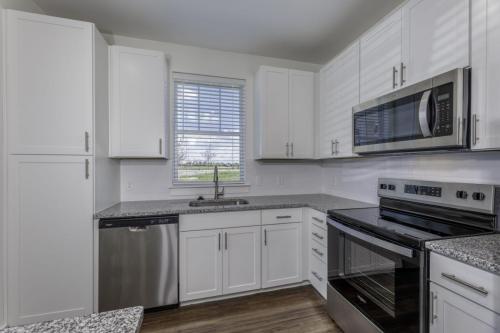 Apartments in Lebanon, IN Modern kitchen with white cabinets, stainless steel appliances including a dishwasher, microwave, and stove, granite countertops, and a window with blinds above the sink.