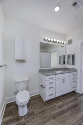 Apartments in Lebanon, IN Modern bathroom with a toilet, white vanity with granite countertop, large mirror, and light fixture above. The floor is made of wood-look vinyl, and the walls are painted white.