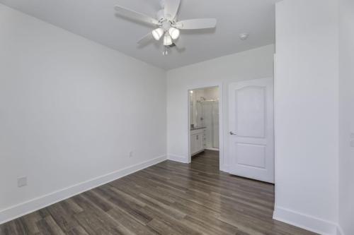 Apartments in Lebanon, IN A room with light colored walls, a ceiling fan with lights, wooden flooring, and an open door leading to a bathroom.