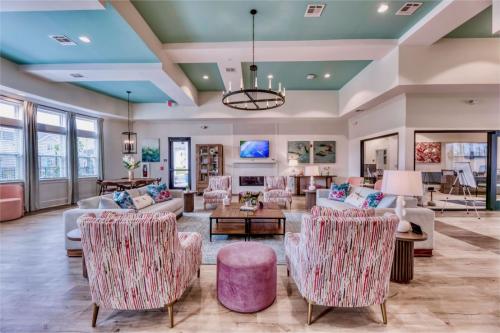 Apartments in Lebanon, IN A modern living room with pastel-colored furniture, including striped armchairs, a round ottoman, and a central coffee table. Large windows line one wall, and a television is mounted above a fireplace.