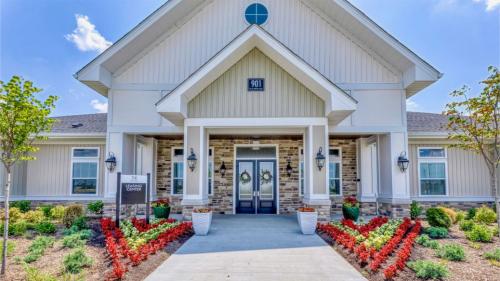 Apartments in Lebanon, IN A light-colored building with double front doors, two potted plants, and a sign that reads Leasing Center surrounded by manicured landscaping and red flowers.