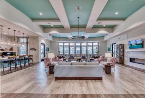 Apartments in Lebanon, IN A spacious, modern living room with a high ceiling, large windows, a centered chandelier, various seating options, a TV, and a kitchen area with pendant lighting.