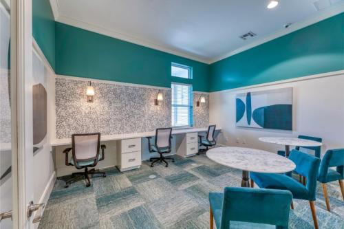 Apartments in Lebanon, IN A brightly lit office space with teal walls featuring multiple workstations with chairs, marble-top tables, modern art on the wall, and large windows allowing natural light.