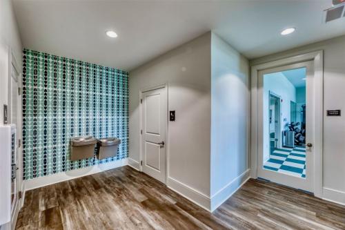 Apartments in Lebanon, IN Modern hallway with wooden floor and patterned green wall, featuring two water fountains. An open door reveals an adjacent room with exercise equipment and checkered floor.