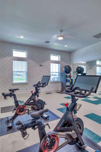 Apartments in Lebanon, IN Two Peloton stationary bikes are placed in a bright, modern fitness room with windows, a large mirror, and exercise equipment against the wall.