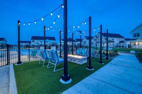 Apartments in Lebanon, IN An outdoor seating area with string lights, a fire pit, and several striped chairs is situated near a swimming pool in a residential complex at dusk.