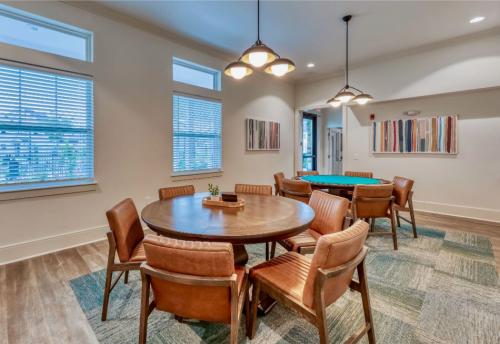 Apartments in Lebanon, IN A modern room with a large round wooden table surrounded by six leather chairs, additional tables with seating, pendant lights, and abstract art on the walls.
