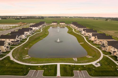 Indiana, Boone County, Lebanon Apartments for rent Aerial view of a suburban neighborhood with houses arranged around an artificial pond with fountains, surrounded by green lawns and paved walkways. See all available apartments for rent at Hickory Cottages in Indiana Boone County Lebanon, Hickory Cottages has rental units ranging from 664-1420 sq ft