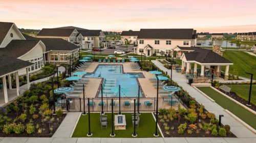 Indiana, Boone County, Lebanon Apartments for rent Aerial view of a residential community pool area with lounge chairs, umbrellas, landscaped gardens, and surrounding houses at sunset. See all available apartments for rent at Hickory Cottages in Indiana Boone County Lebanon, Hickory Cottages has rental units ranging from 664-1420 sq ft
