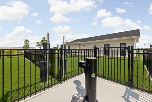 Indiana, Boone County, Lebanon Apartments for rent Fenced dog park area with artificial grass, a building in the background, and a black pet water fountain in the foreground under a partly cloudy sky. See all available apartments for rent at Hickory Cottages in Indiana Boone County Lebanon, Hickory Cottages has rental units ranging from 664-1420 sq ft