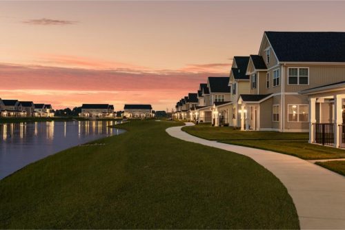 Indiana, Boone County, Lebanon Apartments for rent Row of modern suburban houses with porches lines a curved sidewalk along a small lake at sunset. The sky is partly cloudy with warm evening light. See all available apartments for rent at Hickory Cottages in Indiana Boone County Lebanon, Hickory Cottages has rental units ranging from 664-1420 sq ft