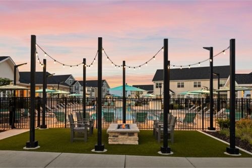 Indiana, Boone County, Lebanon Apartments for rent Outdoor seating area with a fire pit, surrounded by string lights and overlooking a fenced pool with lounge chairs and umbrellas at sunset. See all available apartments for rent at Hickory Cottages in Indiana Boone County Lebanon, Hickory Cottages has rental units ranging from 664-1420 sq ft