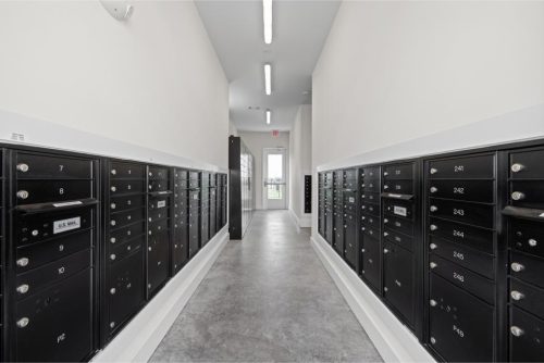 Indiana, Boone County, Lebanon Apartments for rent A hallway with rows of black mailboxes on both sides, white walls, and a concrete floor, leading to a glass door at the end. See all available apartments for rent at Hickory Cottages in Indiana Boone County Lebanon, Hickory Cottages has rental units ranging from 664-1420 sq ft