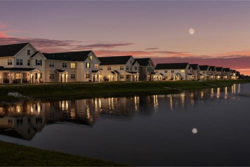 Indiana, Boone County, Lebanon Apartments for rent Row of modern houses with lights on, reflected in a calm pond at sunset, with a visible moon and colorful sky in the background. See all available apartments for rent at Hickory Cottages in Indiana Boone County Lebanon, Hickory Cottages has rental units ranging from 664-1420 sq ft