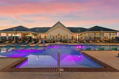 Indiana, Boone County, Lebanon Apartments for rent Outdoor swimming pool with purple lights, lounge chairs, and umbrellas in front of a large clubhouse building at sunset. See all available apartments for rent at Hickory Cottages in Indiana Boone County Lebanon, Hickory Cottages has rental units ranging from 664-1420 sq ft