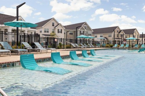 Indiana, Boone County, Lebanon Apartments for rent Outdoor swimming pool with turquoise lounge chairs partially submerged in shallow water, surrounded by more chairs and umbrellas, with residential buildings in the background. See all available apartments for rent at Hickory Cottages in Indiana Boone County Lebanon, Hickory Cottages has rental units ranging from 664-1420 sq ft