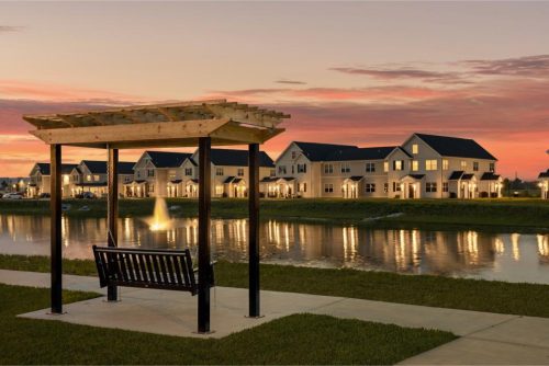 Indiana, Boone County, Lebanon Apartments for rent A wooden swing bench under a pergola overlooks a pond with a fountain, with modern houses and their lights reflected in the water at sunset. See all available apartments for rent at Hickory Cottages in Indiana Boone County Lebanon, Hickory Cottages has rental units ranging from 664-1420 sq ft