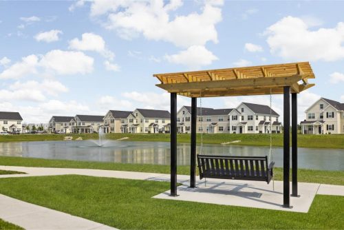 Indiana, Boone County, Lebanon Apartments for rent A wooden porch swing hangs under a pergola, overlooking a pond with a fountain and rows of suburban houses in the background on a sunny day. See all available apartments for rent at Hickory Cottages in Indiana Boone County Lebanon, Hickory Cottages has rental units ranging from 664-1420 sq ft