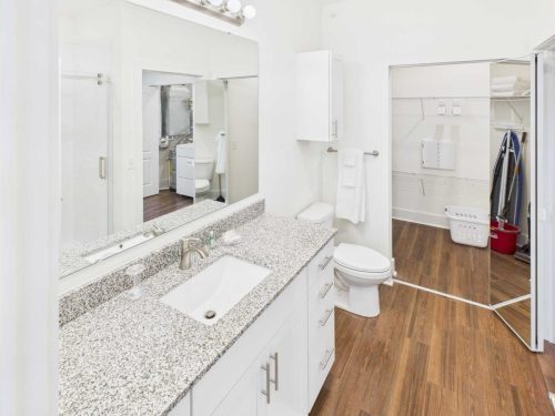 Indiana, Boone County, Lebanon Apartments for rent Modern bathroom with granite countertop, white cabinets, wide mirror, toilet, wooden floor, and a view into a walk-in closet with shelves and laundry basket. See all available apartments for rent at Hickory Cottages in Indiana Boone County Lebanon, Hickory Cottages has rental units ranging from 664-1420 sq ft