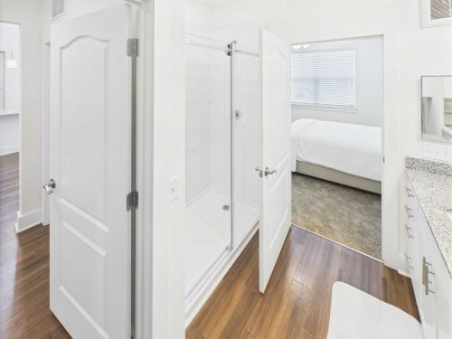 Indiana, Boone County, Lebanon Apartments for rent A modern bathroom with a glass shower, granite countertop, wood flooring, and white doors leading to a bedroom with a bed and carpeting. See all available apartments for rent at Hickory Cottages in Indiana Boone County Lebanon, Hickory Cottages has rental units ranging from 664-1420 sq ft