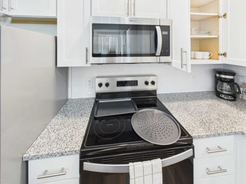 Indiana, Boone County, Lebanon Apartments for rent A modern kitchen countertop with an electric stove, microwave, coffee maker, and open cabinet displaying dishes. Baking trays sit on the stove. See all available apartments for rent at Hickory Cottages in Indiana Boone County Lebanon, Hickory Cottages has rental units ranging from 664-1420 sq ft