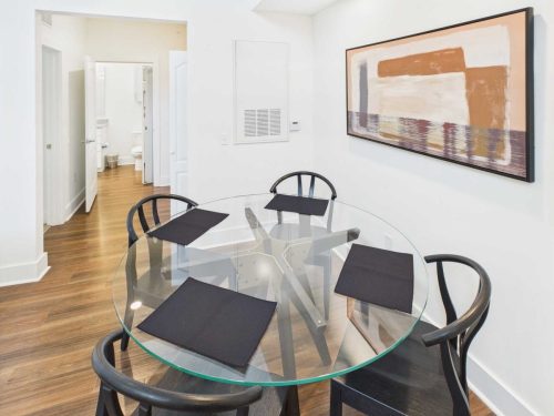 Indiana, Boone County, Lebanon Apartments for rent A glass dining table with four black chairs and black placemats in a modern room with wood flooring and abstract art on the wall; bathroom visible in the background. See all available apartments for rent at Hickory Cottages in Indiana Boone County Lebanon, Hickory Cottages has rental units ranging from 664-1420 sq ft